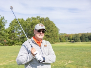 A man wearing Buffalo State apparel and holding a golf club