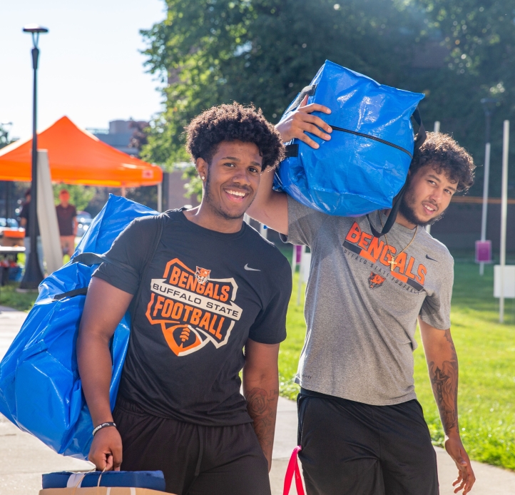 Two smiling students moving into the dorm